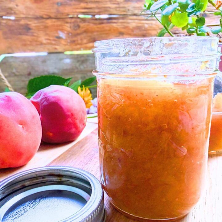 A jar of peach jam. there are two peaches in the background.