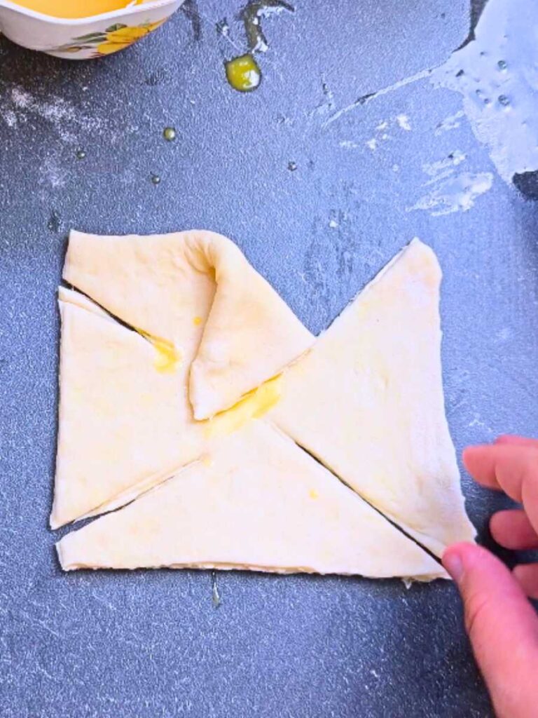 A woman is folding danish dough into a pinwheel shape.