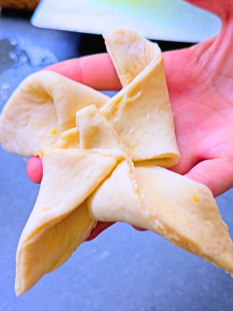 A woman is holding up dough folded into a pinwheel shape.