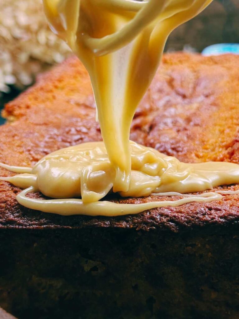 A woman is drizzling brown sugar icing on a red current loaf cake.
