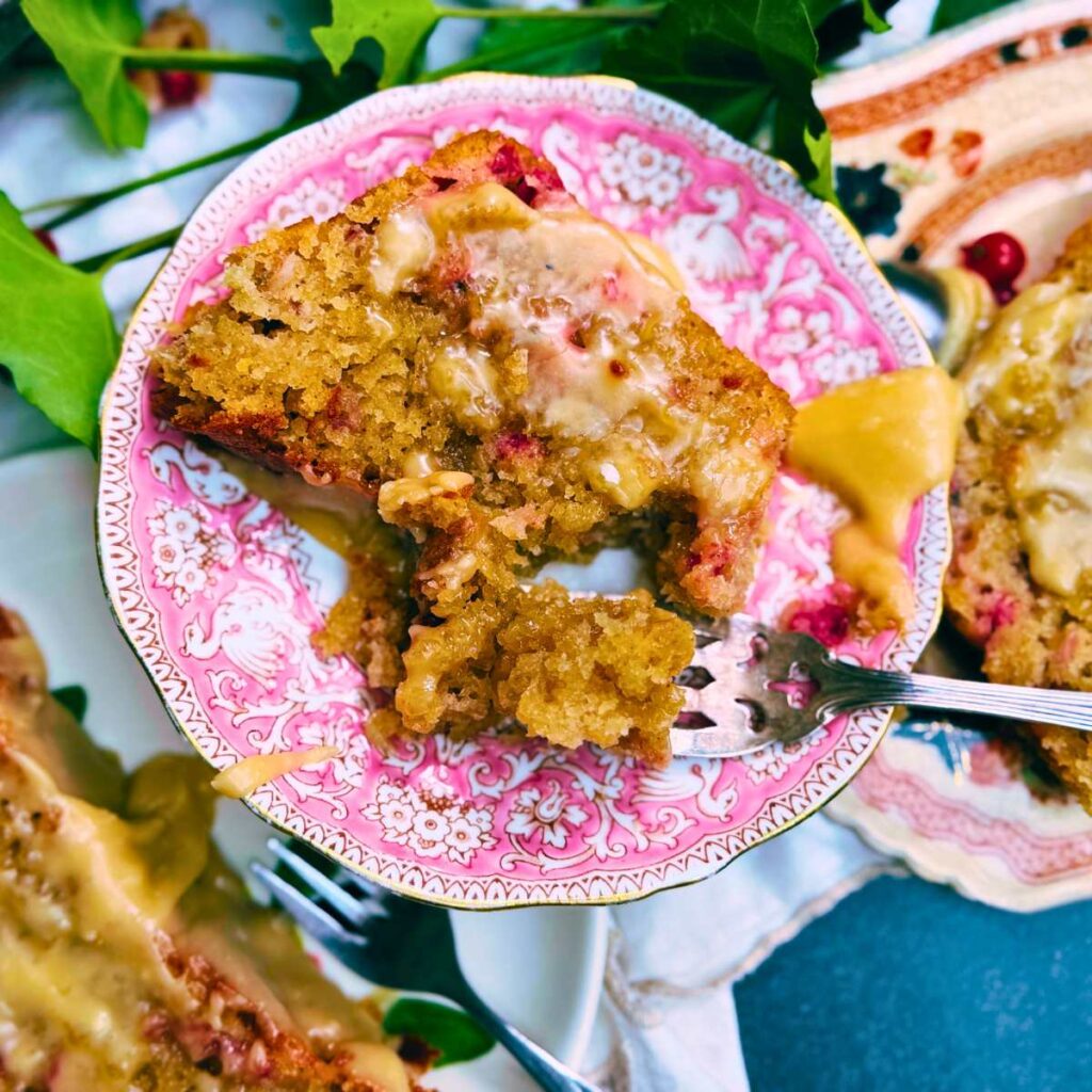 A pink plate with a slice of red current loaf cake. There is a fork on the plate.