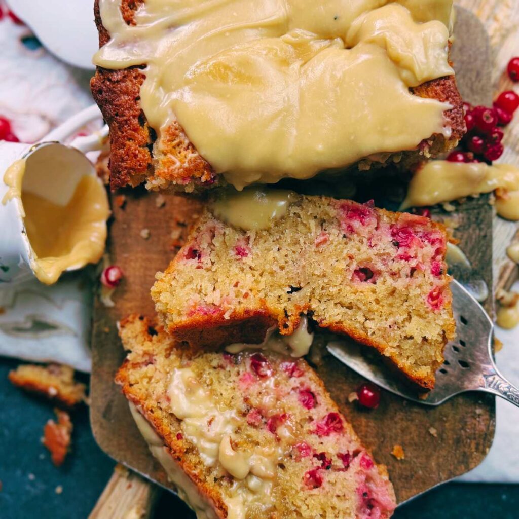 An overhead view of a red current loaf cake with brown sugar icing. Two pieces have been sliced to show the inside of the cake.