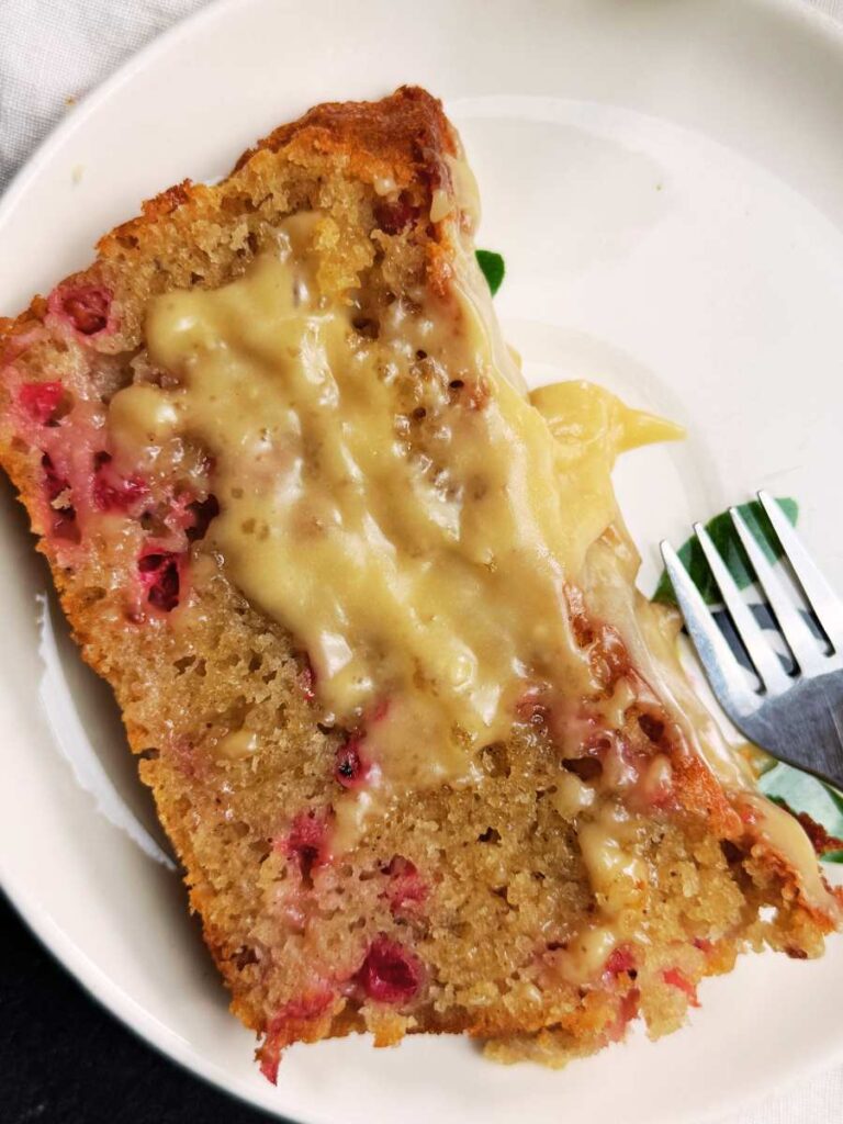 A slice of red current loaf cake with brown sugar icing on a white plate.