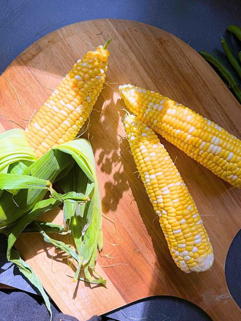 Three ears of corn. One is partially husked.