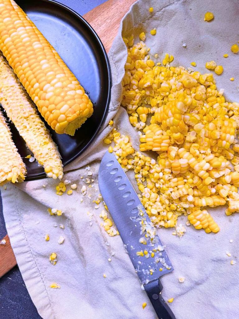 A black plate with some ears of corn. Two have the kernes cut off. The kernels are on a cloth to the side.
