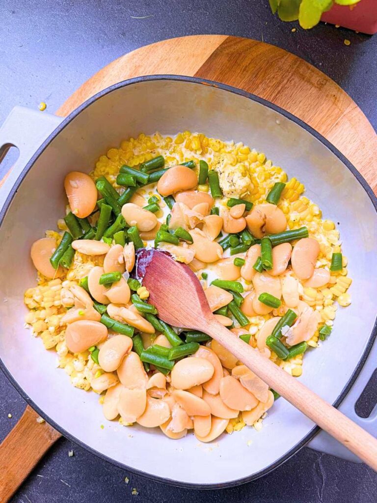 A grey sauce pot with corn, beans, butter, and cream inside.