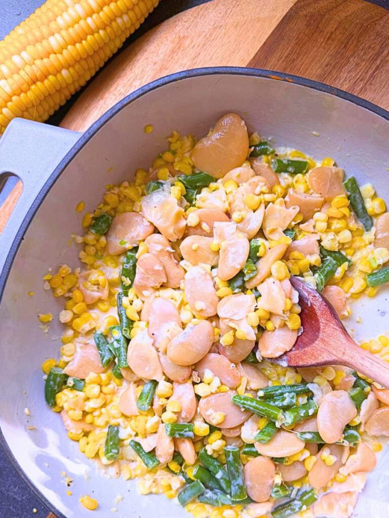 A large grey pot with corn and bean succotash and a wooden spoon inside.
