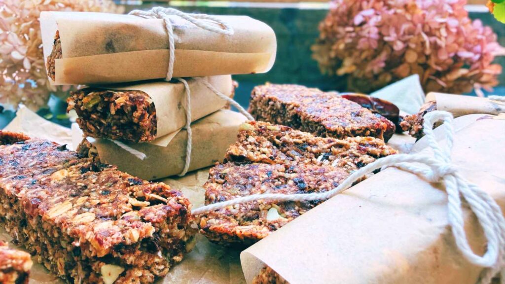 A collection of granola bars. Some are wrapped in parchment paper. Three are stacked in the back.