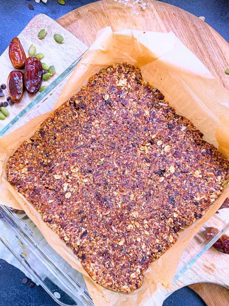 A granola bar mixture pressed into a parchment lined square glass casserole dish.