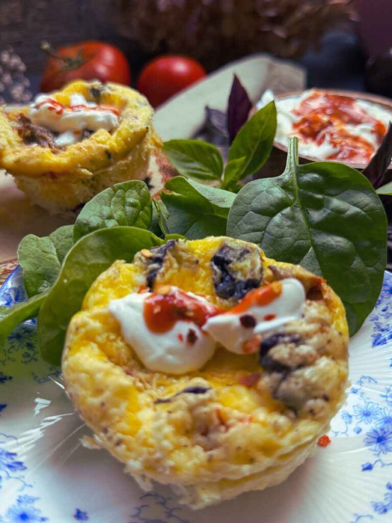 A tomato basil muffin tin frittata with cream and hot sauce on top.