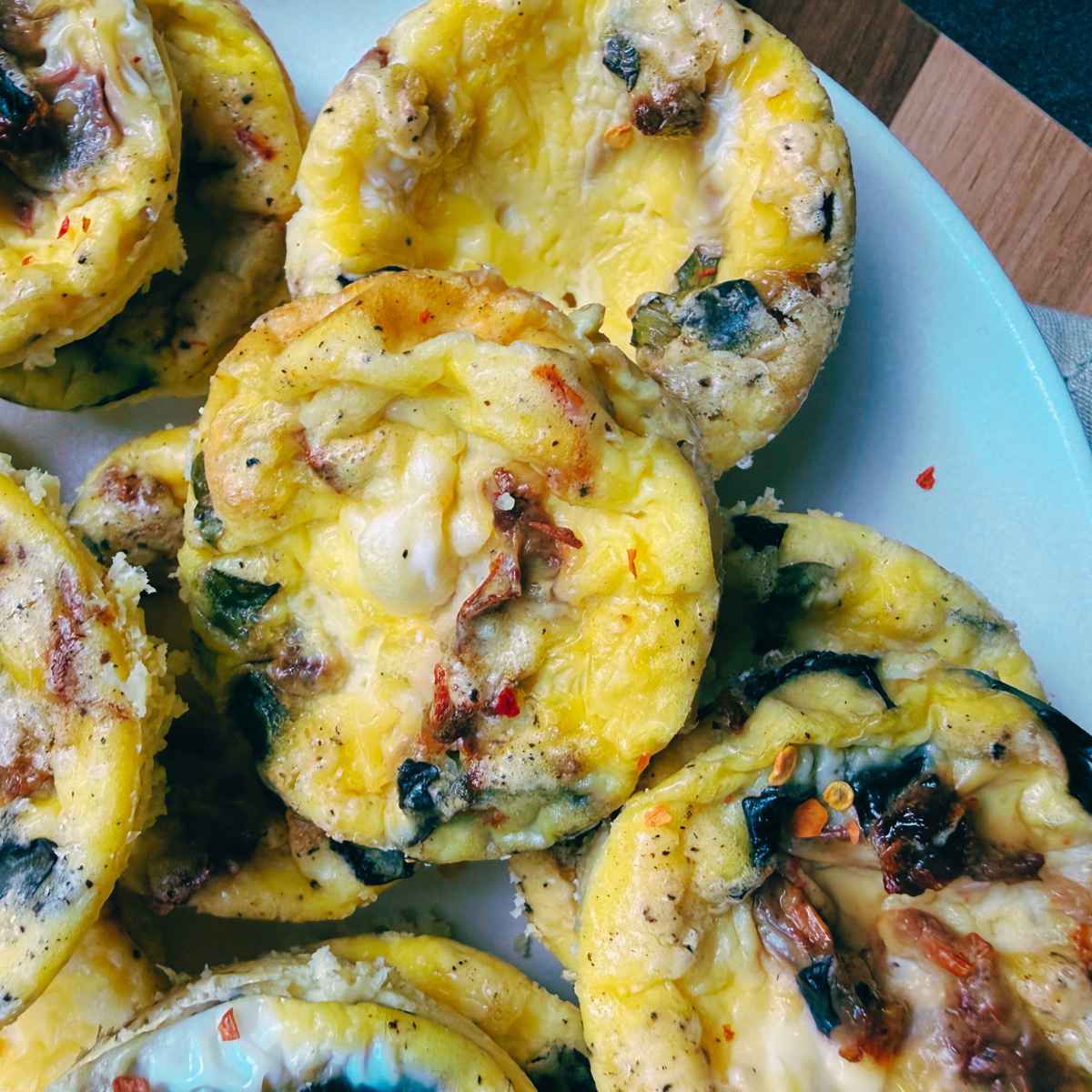 A white plate piled with tomato basil muffin tin frittatas.