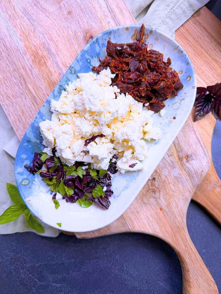 A blue plate with chopped sun dried tomato, feta, and basil.