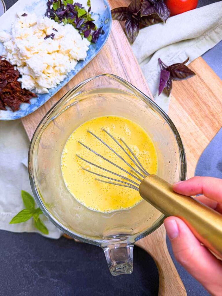 A woman whisking an egg mixture in a glass measuring cup.