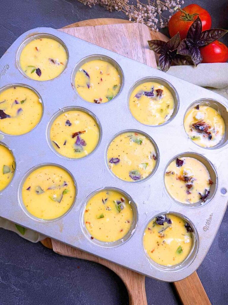A muffin tin filled with tomato basil frittata mixture.