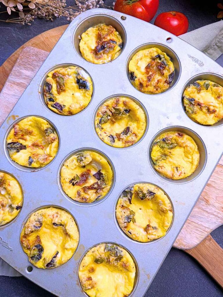 A muffin tin with baked tomato basil muffin tin frittatas inside.