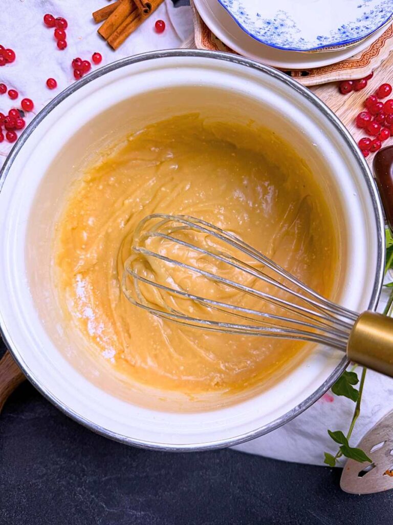 Brown sugar icing in a white sauce pot. There is a whisk inside.