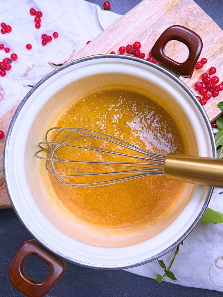 Melted butter and brown sugar in a white sauce pot. There is a whisk inside.