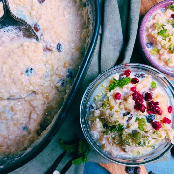 A baked rice pudding in a black baking dish. There are two servings off to the side. They are topped with nuts and berries.