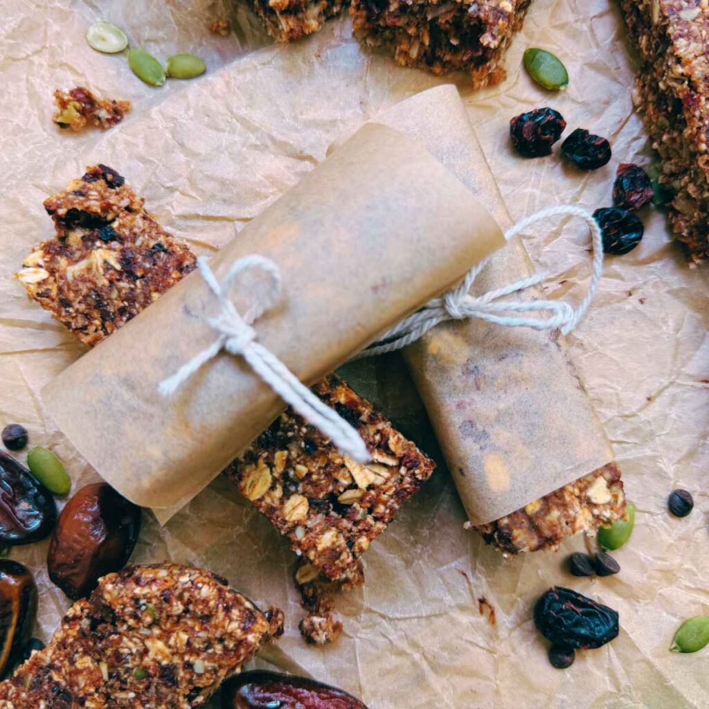 Granola bars on a piece of parchment paper. Two are wrapped in parchment paper.