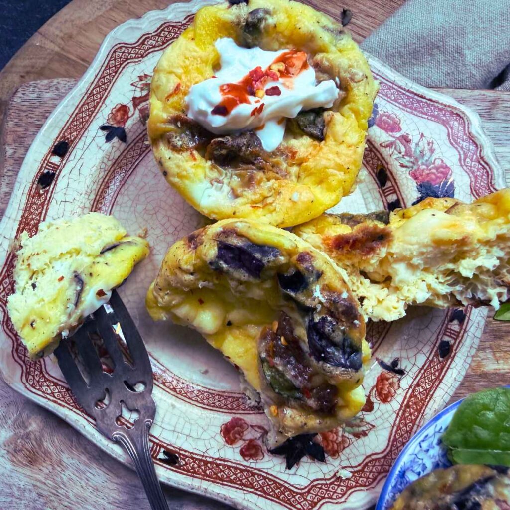 Two muffin tin frittatas on a brown plate. One is split in half.