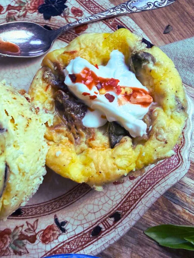 A muffin tin frittata on a brown plate. There is cream and hot sauce on top.