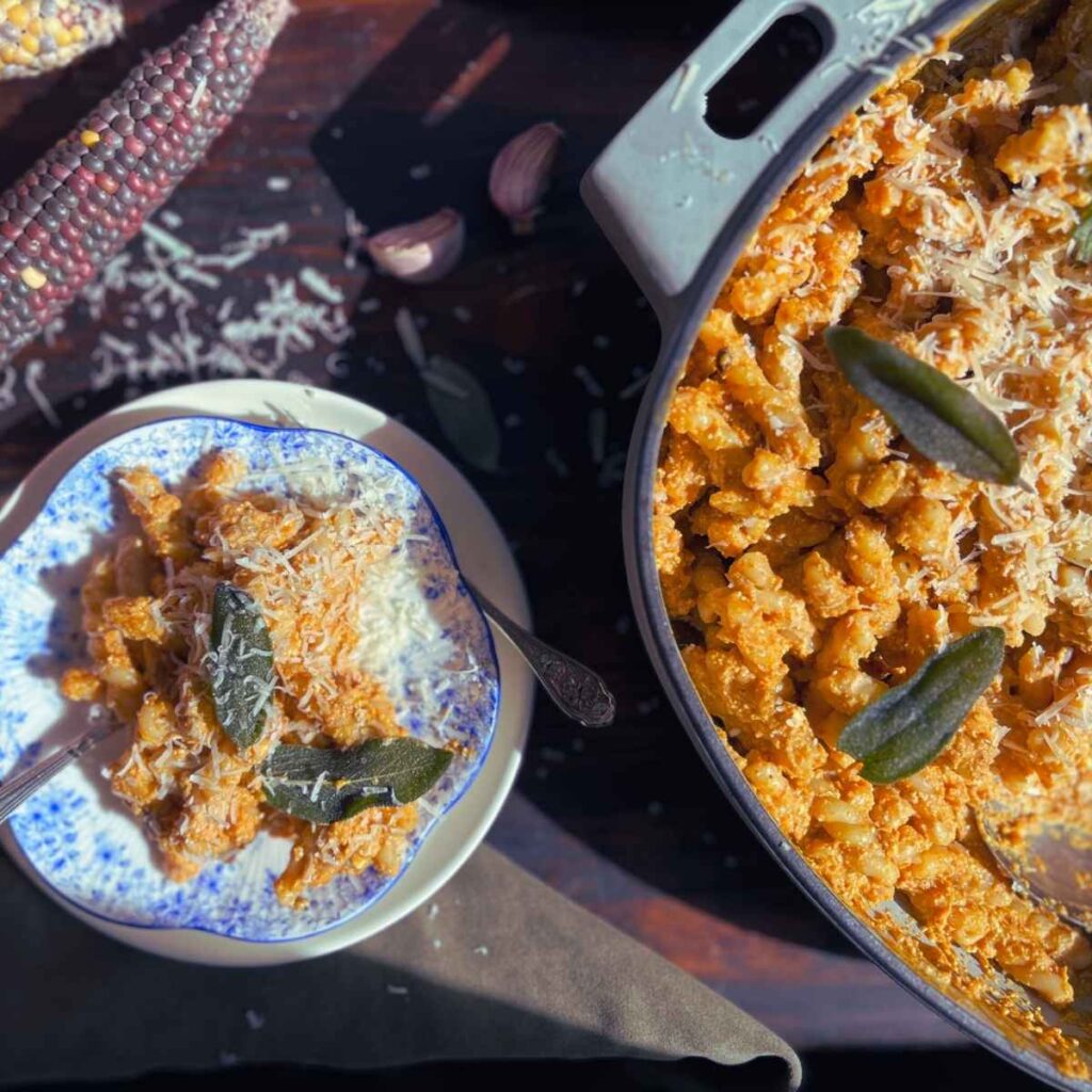 A small plate of pumpkin pasta with sage leaves on top. There is more in a Dutch oven off to the side.