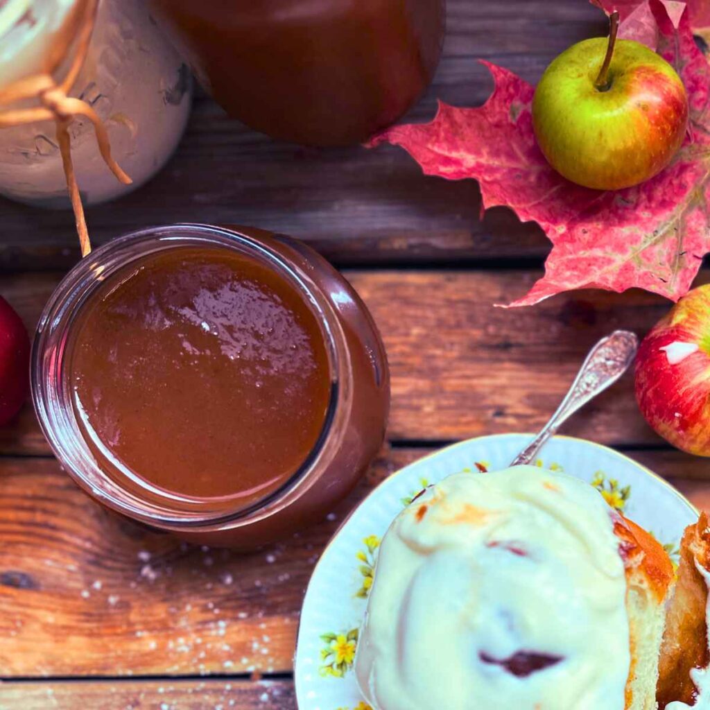 A jar of apple butter with a cinnamon roll covered in icing off to the side.