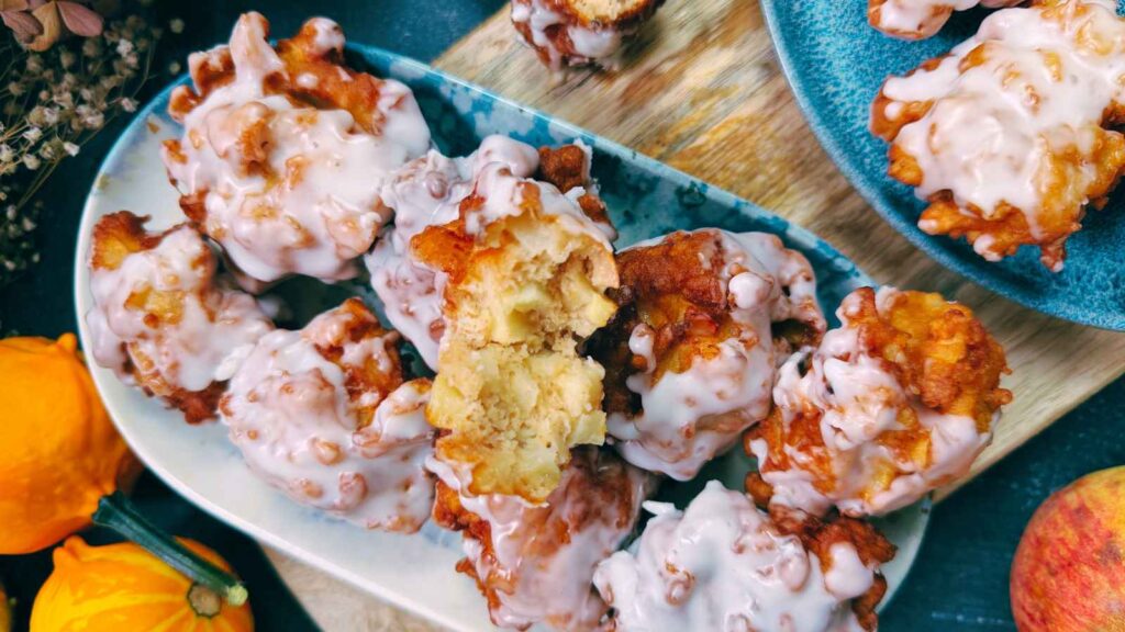 A blue and white dish filled with apple fritters. There are more on a blue plate to the side.