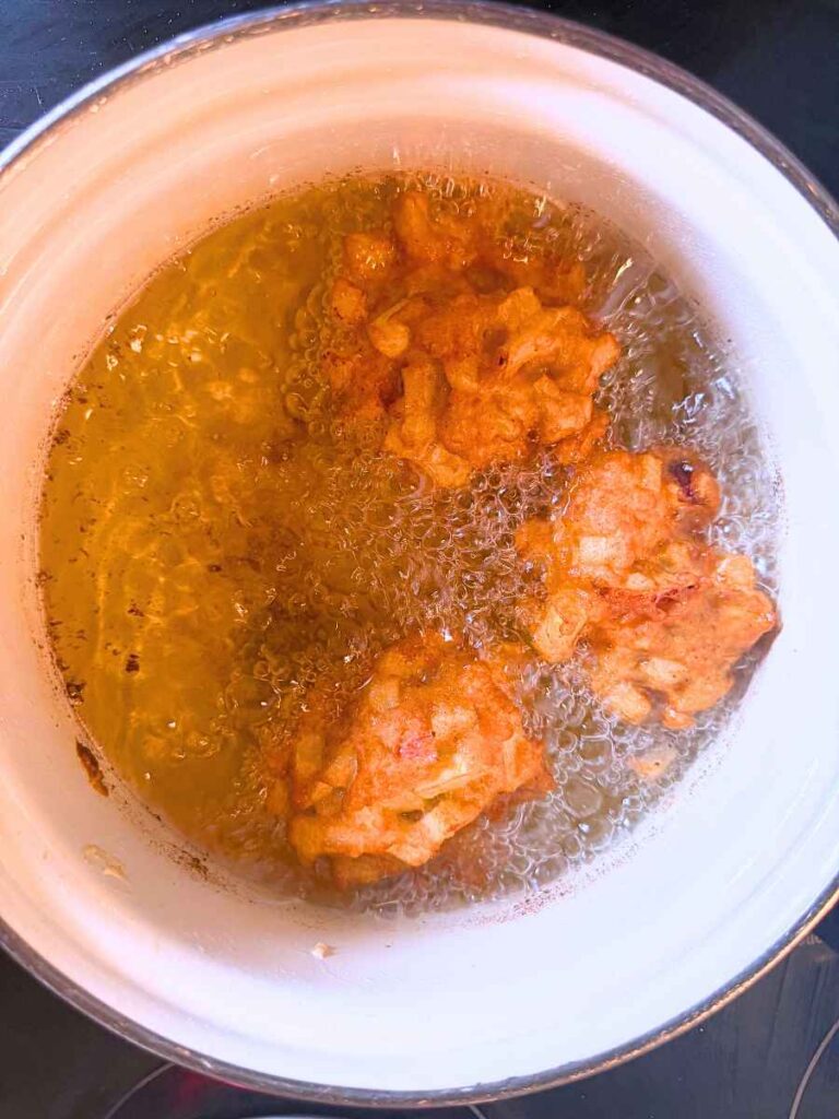 Cooked apple fritters in a white sauce pot of hot oil.