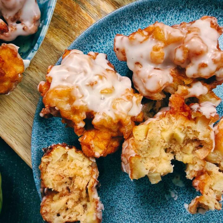 An overhead view of apple fritters on a blue plate. One is broken in half to show the inside.