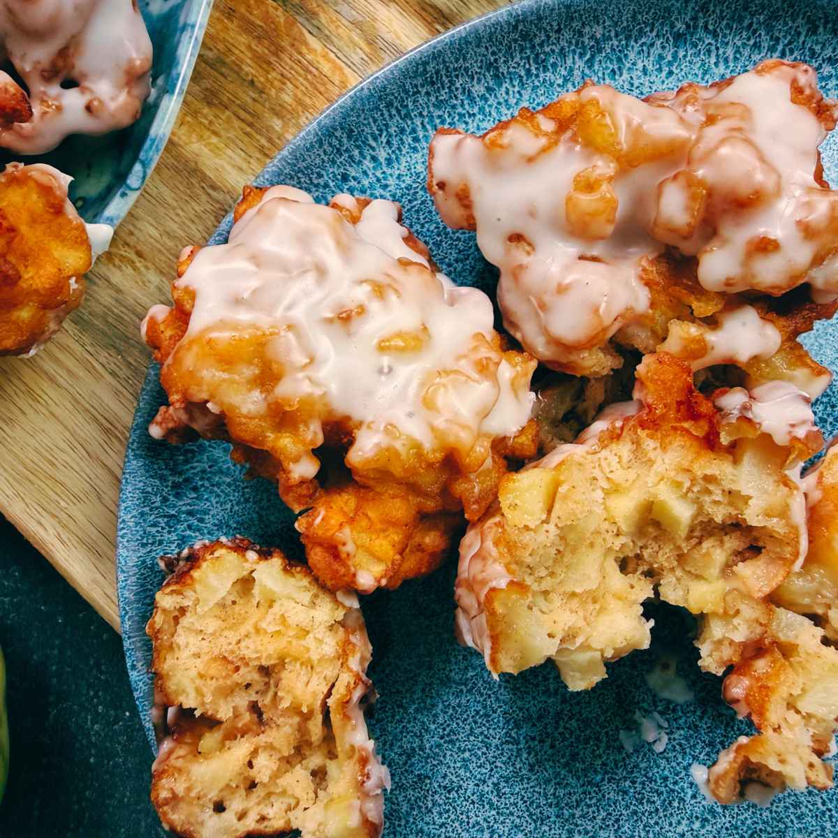 An overhead view of apple fritters on a blue plate. One is broken in half to show the inside.