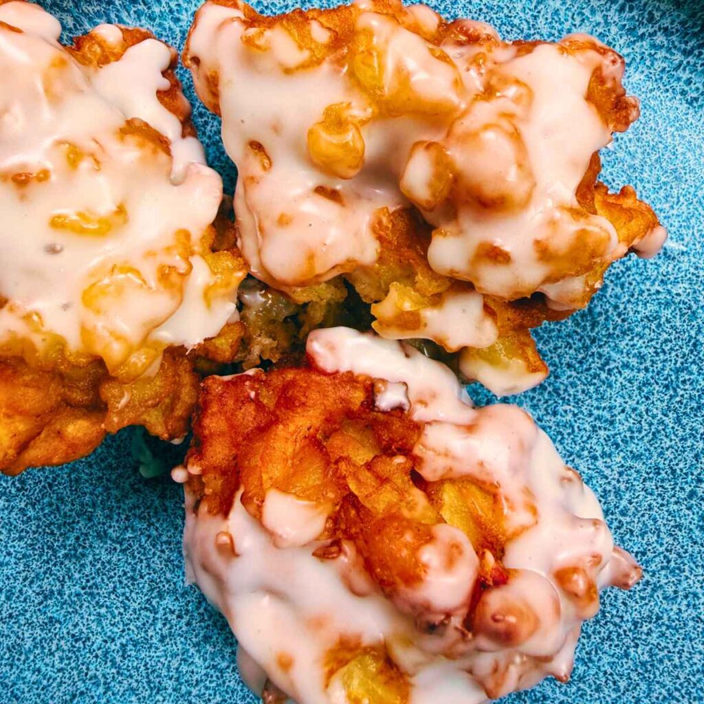 Three glazed apple fritters on a blue plate.