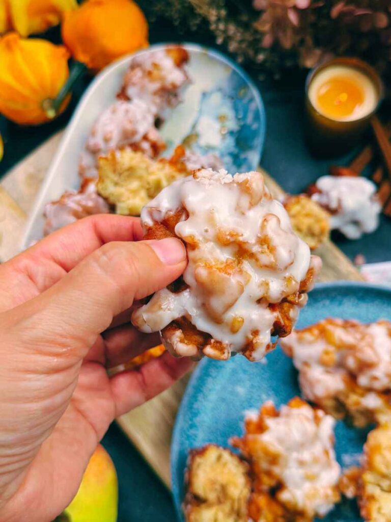 A woman is holding an glazed apple fritter.