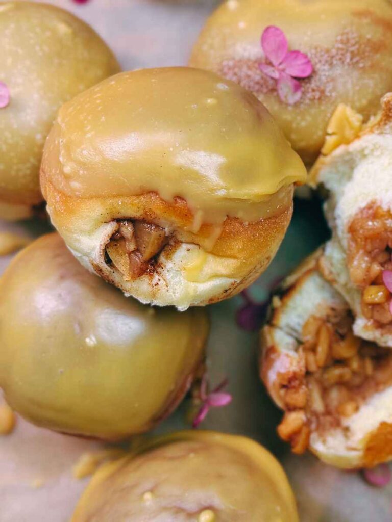Some apple stuffed glazed doughnuts. One is split in half to show the inside filling.
