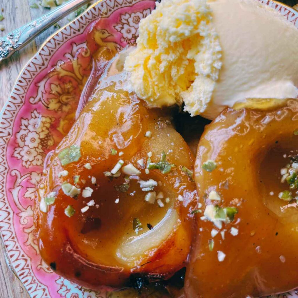 A pear cut in calf on a pink plate covered in caramel and garnished with nuts and ice cream.