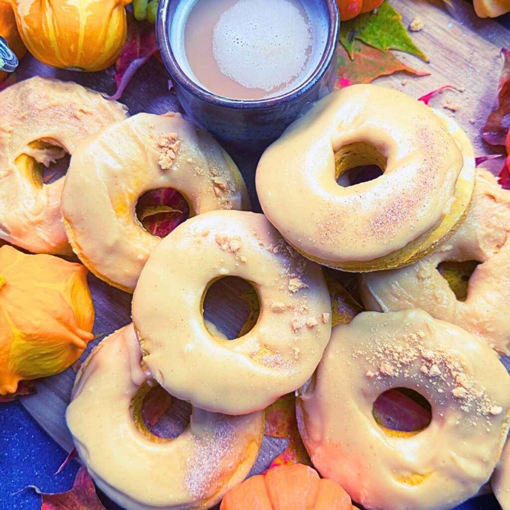 A collection of pumpkin doughnuts dipped in a caramel icing. There is a cup of coffee in the background.