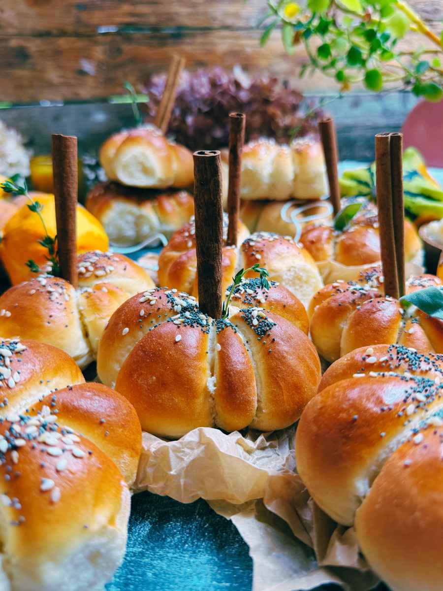 A side view of pumpkin shaped dinner rolls. Each has a cinnamon stick representing the stem.