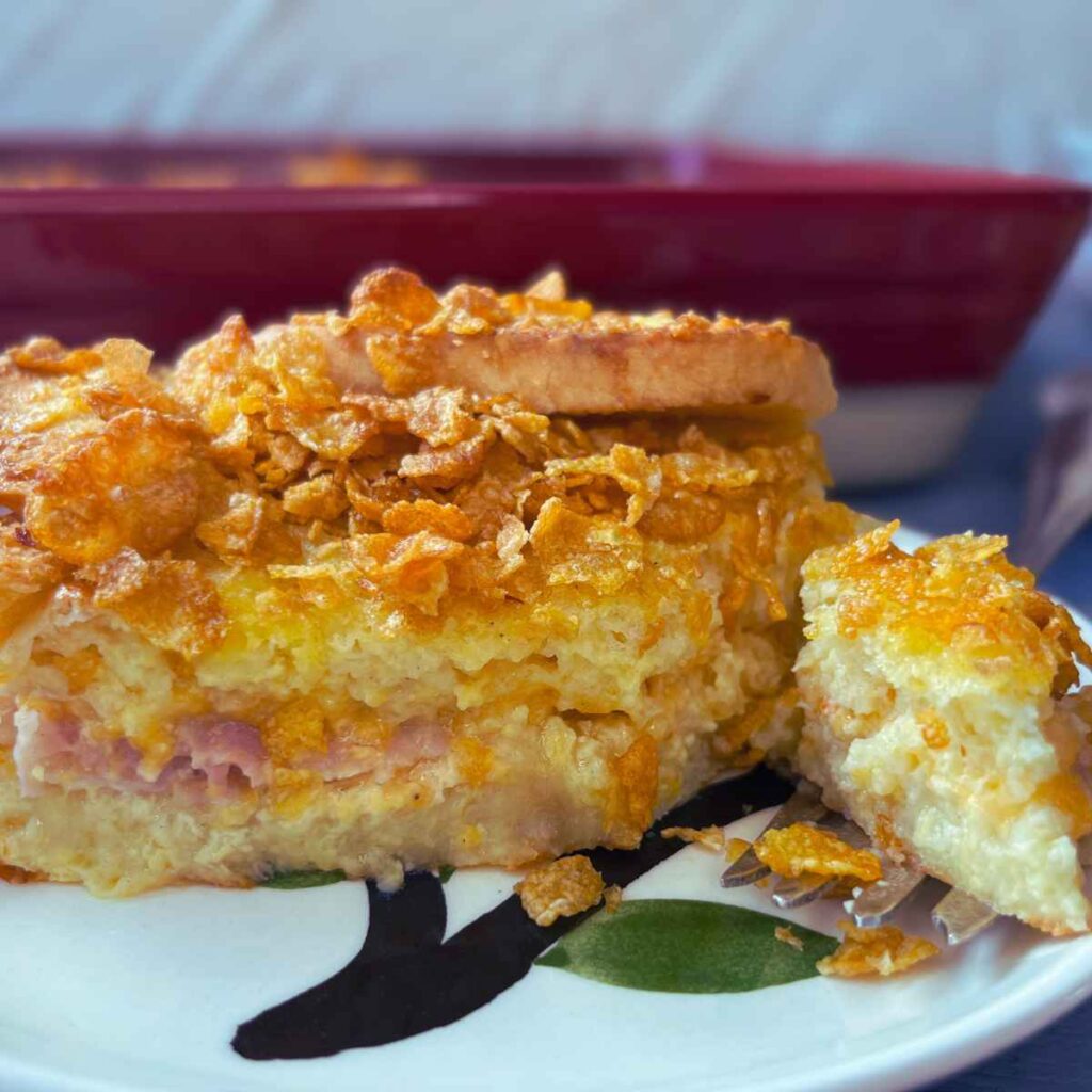 A side view of a breakfast strata. There is more in a red casserole dish in the background.