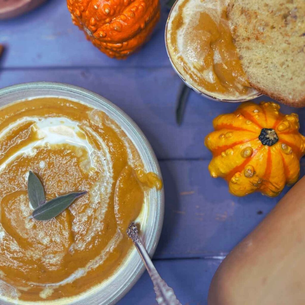 Two bowls of butternut squash soup. One has sage leaves on top and one has a slice of toast.