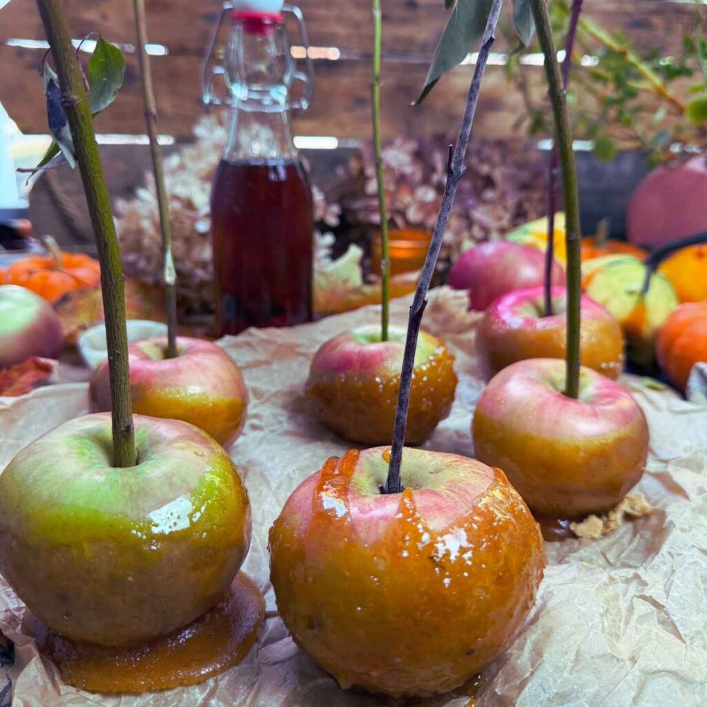 Maple dipped apples. They have sticks inside and a bottle of maple syrup in the background.