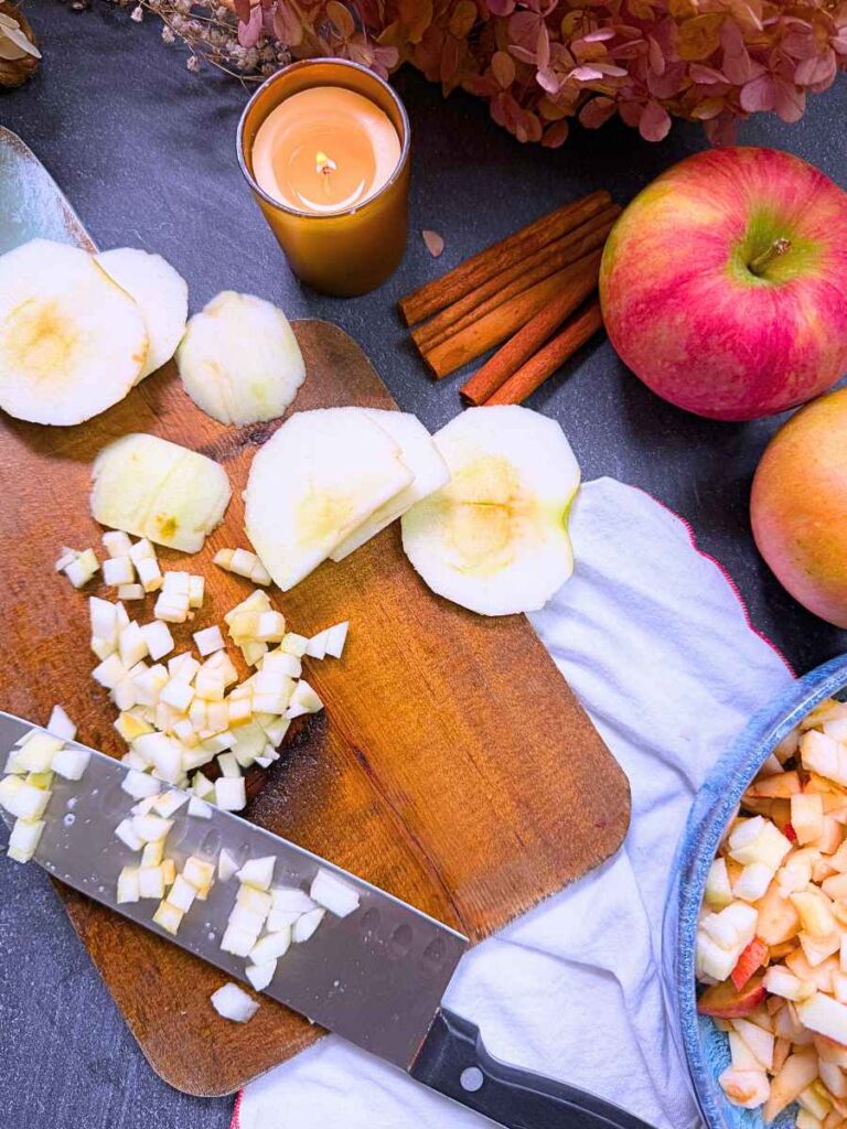 Cut apples in a small dice on a wooden cutting board. There is a knife off to the side.