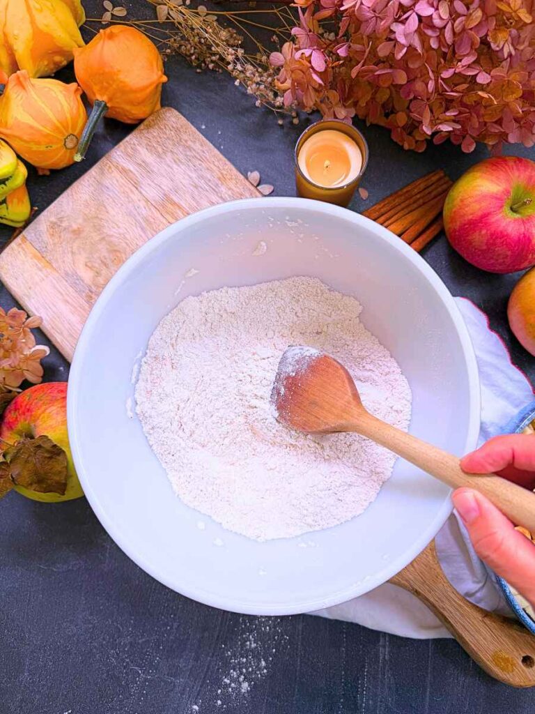 A white bowl with dry ingredients being mixed by a woman holding a wooden spoon.