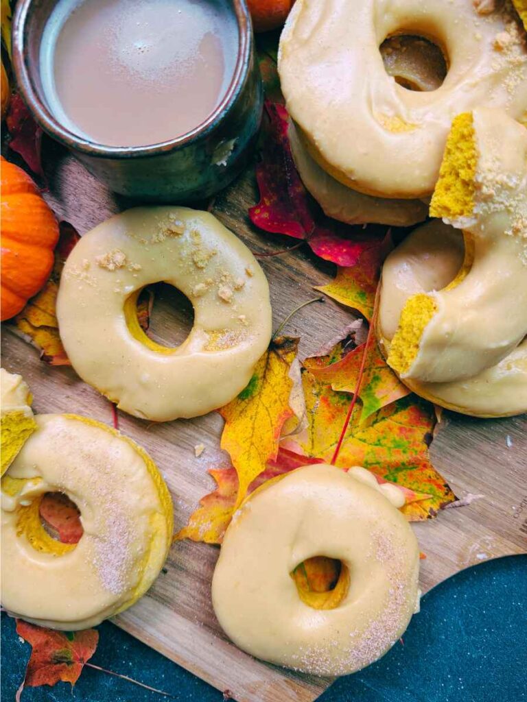 Three baked pumpkin doughnuts with a caramel dip. There is a cup of coffee in the background.