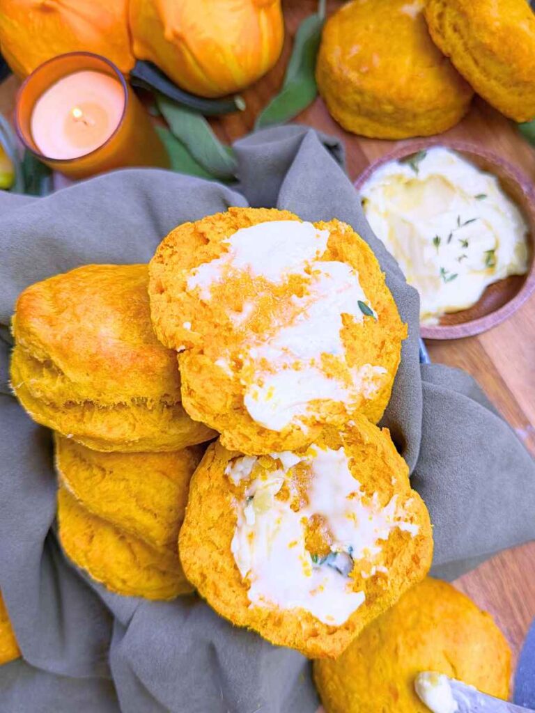 Pumpkin biscuits in a linen lined basket. One is split in half and buttered.