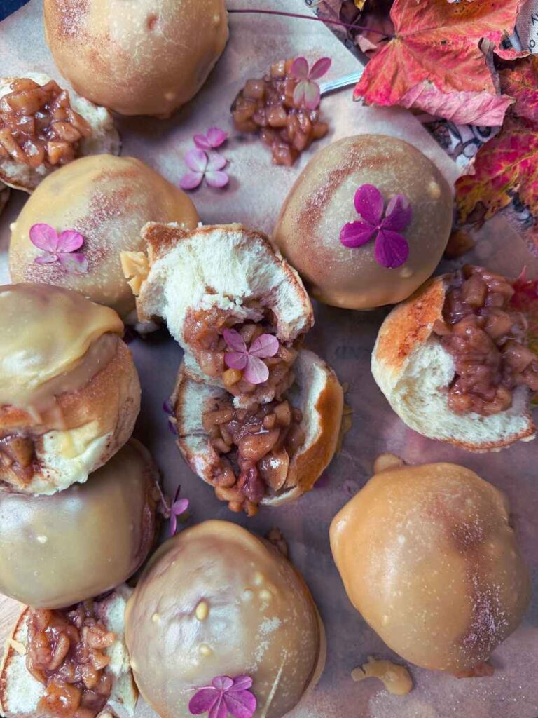 A collection of baked apple stuffed doughnuts with a caramel glaze. Some are split in half to show the inside of the doughnut.