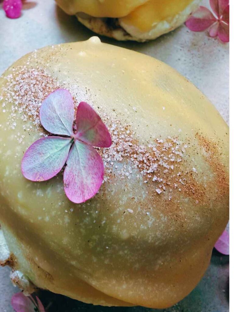 A close up look at a dipped baked doughnut. There is a small pink flower on top.