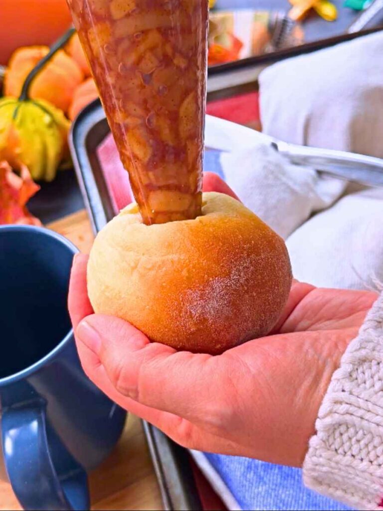 A woman is filling a baked doughnut with a apple filling in a piping bag.