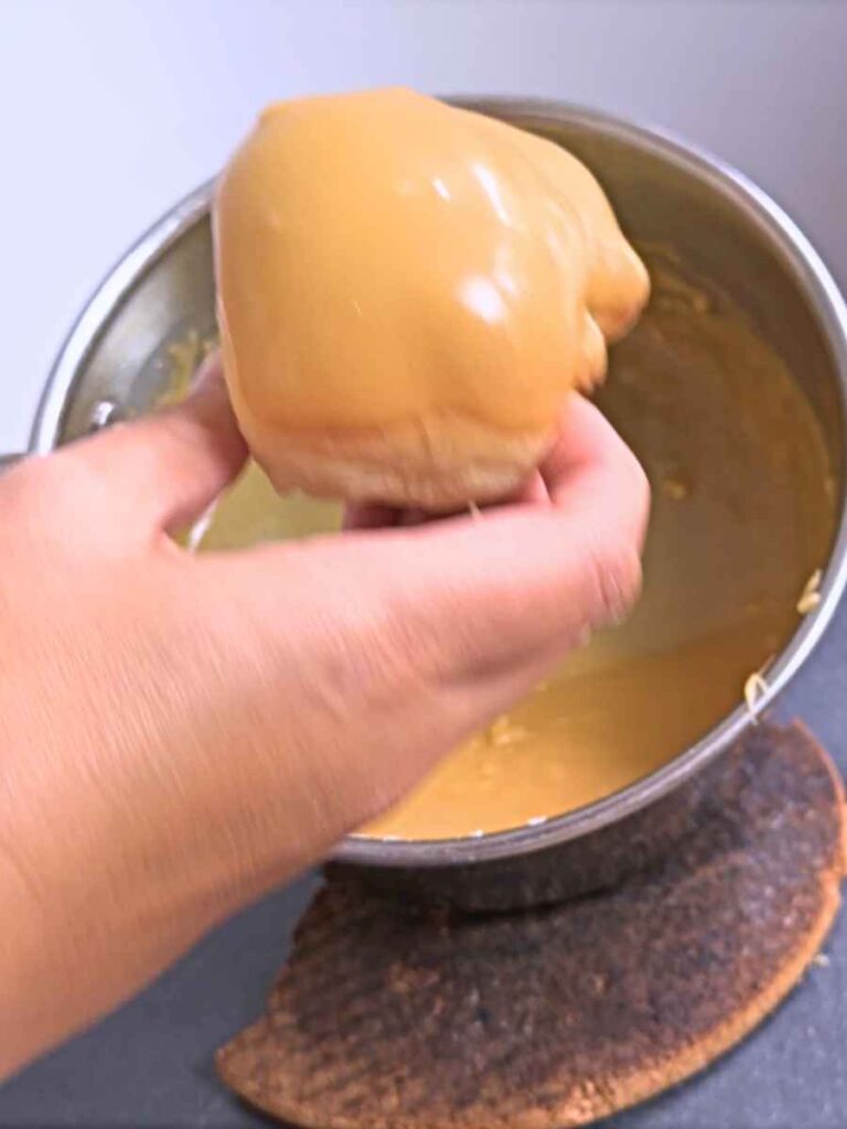 A woman is holding up a freshly dipped doughnut with a caramel glaze on top.