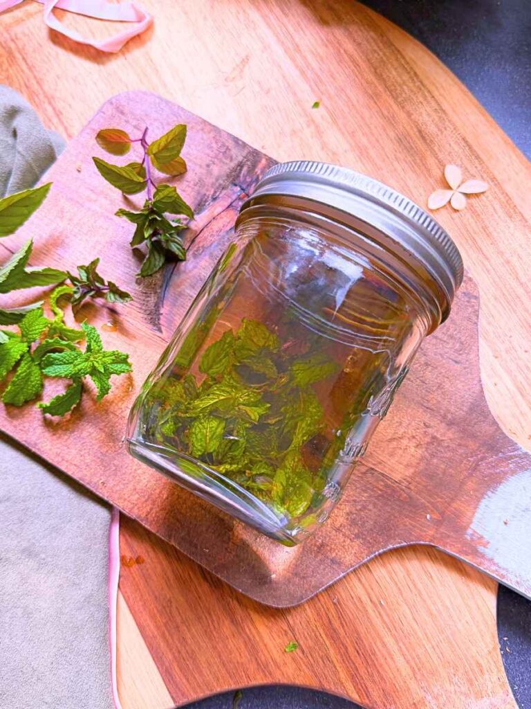 A sealed glass canning jar on its' side. It has mint leaves and vodka inside.