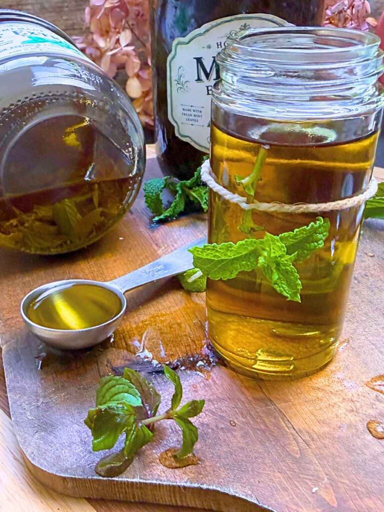 Three jars for fresh mint extract. One is tipped on its' side. One has a leaf tied to it. There is a teaspoon measure on extract to the side.